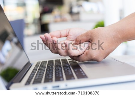 Close up woman holding and pressing or touching her hand while working with laptop in the office. Numbness or pain on hand concept.
