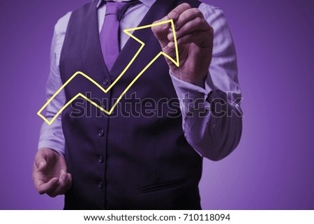 Shooting in the Studio .A businessman in a waistcoat ,shirt and tie on a purple background draws growth arrow