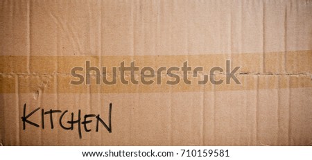 Brown cardboard moving box with packing tape and word Kitchen written in black pen