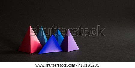 Abstract colorful geometrical composition. Three-dimensional prism pyramid objects on black paper background. Pink blue violet colored solid figures, soft focus photo. Copy space