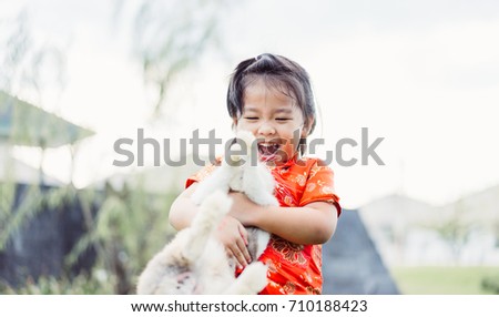 Happy Little asian girl in chinese traditional dress smiling and holding big rabbit and showing front teeth with big smile.Happy chinese new year and chinese moon festival concept.