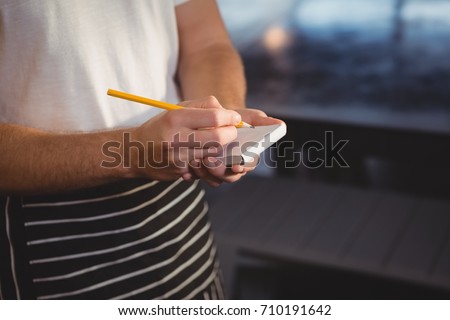 Mid section of waiter taking order while standing at cafe Royalty-Free Stock Photo #710191642