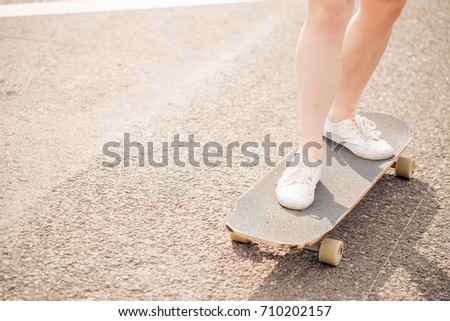 lifestyle, longboarding and people concept - female legs riding on longboard along road