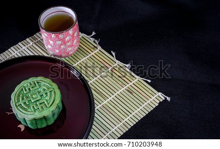 Minimalist layout of a mid-autumn festival theme, comprising the traditional moon cake and a pretty tea cup on a bamboo mat. Space for words available, suitable for background or wallpaper.