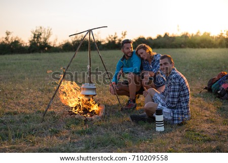 Friends camping at sunset with kettle