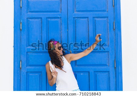 young beautiful happy woman taking a selfie with her mobile phone over a blue door background. Summer. Lifestyle