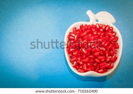 The Jewish New Year Rosh Hashanah concept - apple shaped plate with red pomegranate seeds on a blue background. Rosh Hashanah greeting