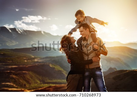 Happy family of father mother and little son having fun in sunset mountains