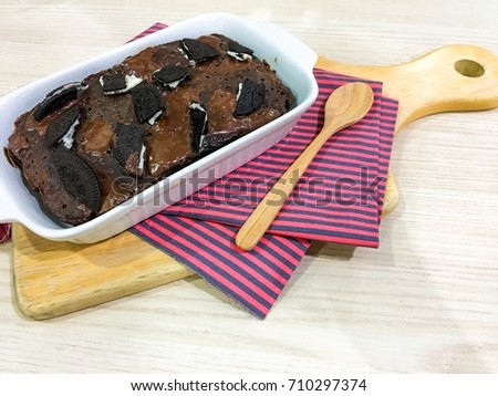 Chocolate cake on board with a spoon over a napkin on white wooden table. 
