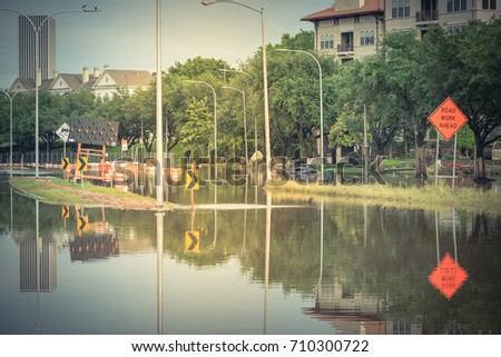 High water rising at Allen Parkway with road warning signs. Residential buildings and downtown Houston in background under cloudy sky. Heavy rains from storm cause many flood. Swamp car. Vintage tone