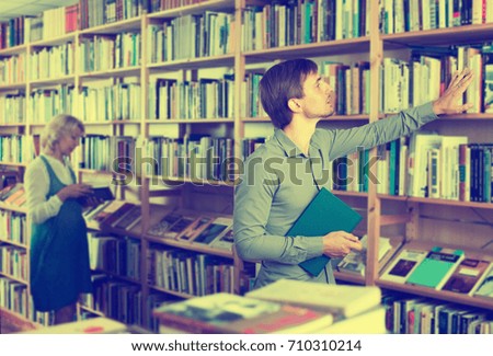 Young positive man searching for new book on shelves in book store