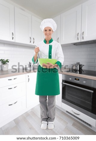 young woman in chef uniform mixing something in green plastic bowl in modern kitchen