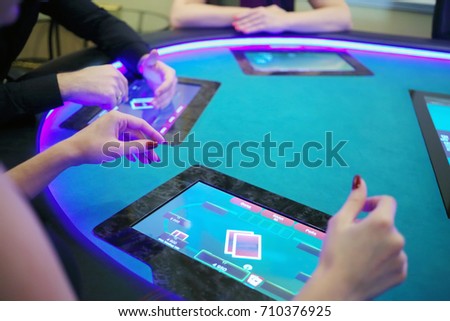 Hands of two women and man play poker in casino with electronic table, focus on woman hand