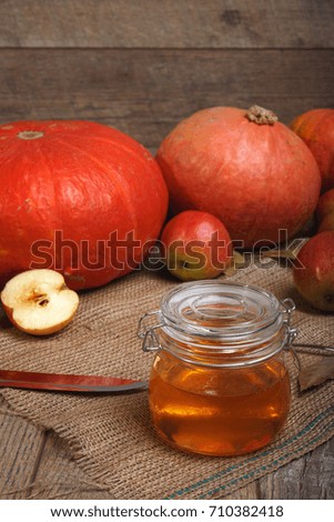 Bright fresh pumpkins, cut apples and a glass jar full of honey on a wooden background. Autumn harvest.