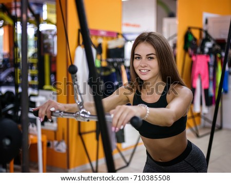 A photo of a girl with a perfect body doing sporty exercises with a simulator on a gym background. Fitness concept.