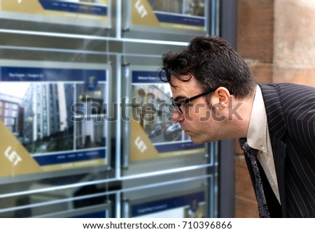 A business man looking at houses / flat for sale in estate agent window.