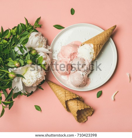 Flat-lay of pastel pink strawberry and coconut ice cream scoops, sweet cones on white plate and white peony flowers bouquet over pastel pink background, top view, copy space, square crop