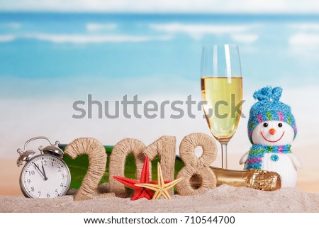 New Year inscription 2018, a bottle and a glass of champagne, snowman, alarm clock and starfish on the sand.