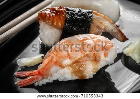 Japanese sushi made of rice and sea bass, shrimp and smoked eel with chopsticks on a black plate. The horizontal frame.