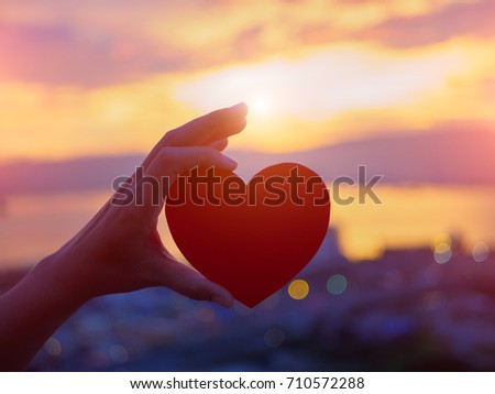 Silhouette hand holding beautiful heart during sunset background. Happy, Love, Valentine's day idea, sign, symbol, concept.