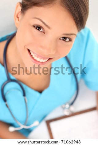 Medical professionals: Woman nurse smiling while working at hospital writing medical report. Young multiracial asian / caucasian female health care worker.