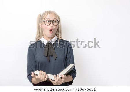 Teenage girl with long blonde hair in glasses and a school uniform with a book in her hands surprised opened her mouth