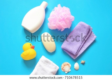 Flat lay bath products. Shampoo bottle, yellow rubber duck, soap, pink sponge puff, purple and white towels, seashells on a blue background. Flat lay shower items. Bathroom stuff. Top view photo