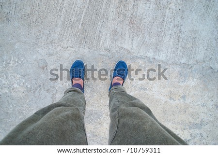 Women wear gray trousers and dark blue sneakers, stand on concrete floor. She took her selfie shot, pants and shoes on her own as a view from above.
