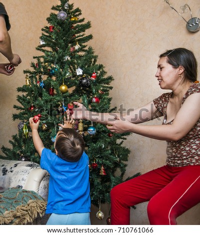 Portrait of happy mother, father and back view boy  decorating Christmas tree inside room. Baby boy helping asian mother decorate christmas tree