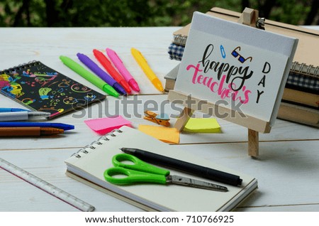 Happy teacher day concept. Lovely greeting card for teachers writing in calligraphy handwriting style on white paper and wooden frame with students and school supplies on white wood desk background