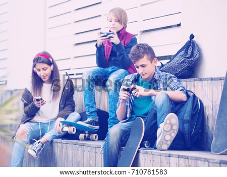 Three teenagers with smartphones in autumn day outside