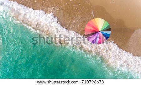 Colorful of umbrella on the beach and foam of sea wave from top eye view photo in outdoor sunlight lighting.
