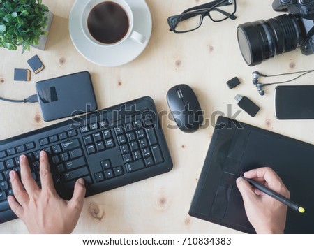 top view work space of photographer hand or creative designer hand with digital camera, computer keyboard, memory card, graphic tablet, coffee cup, mouse on wooden table.