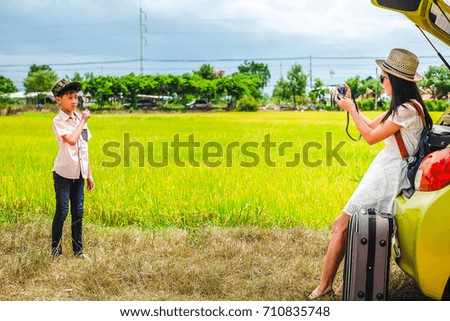 Woman traveler take photo her son and view of rice field with her camera on vacation.
