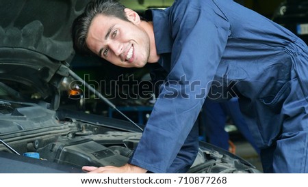 In a garage, a mechanic after having checked and checked the oil and engine at the car smiles because the car has been repaired successfully. Concept of: security,safety, insurance and professionalism