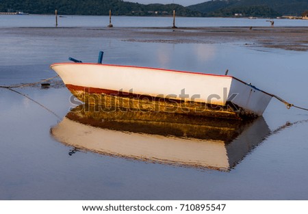 White dinghy  parked on the beach at a time when the sea water dropped. There is a reflection of water at sunrise.
