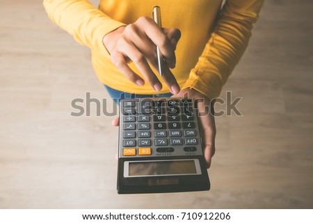 Woman entrepreneur using a calculator with a pen in her hand, calculating financial expense at home office Royalty-Free Stock Photo #710912206