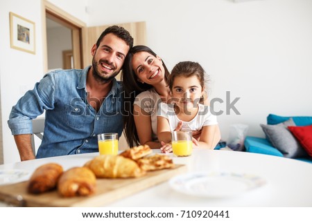 Husband and wife with they little daughter sitting at the kitchen table.Family portrait. Royalty-Free Stock Photo #710920441