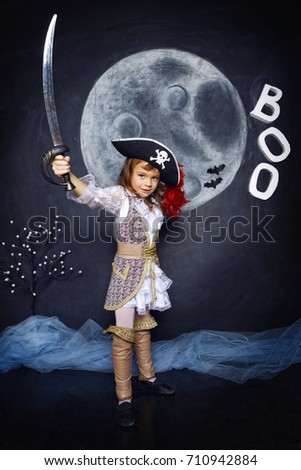 Little girl dressed in pirate costume on a black background with a moon image in a studio with Halloween decorations