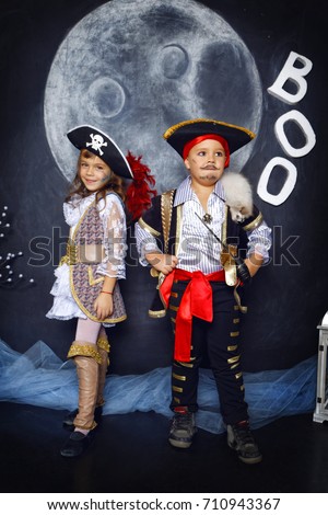 Little boy and girl dressed in pirate costumes on a black background with a moon image in a studio with Halloween decorations
