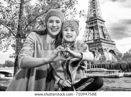 Autumn getaways in Paris with family. Portrait of happy mother and daughter tourists on embankment near Eiffel tower in Paris, France showing heart shaped hands