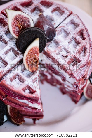 Delicious pink waffle cake with cream cheese filling with figs and chocolate cookies on top, rustic old wooden table background
