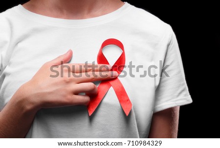 A female with a red ribbon on a white T-shirt on a black background. Modern treatment and healthcare. AIDS awareness concept. Royalty-Free Stock Photo #710984329