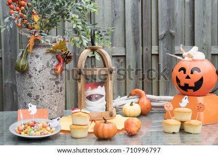Halloween decorations on wooden table with cake, pumpkin, candy, orange flowers and mummy 