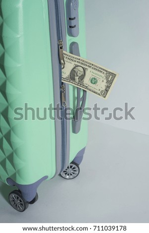 dollar bill and a suitcase on wheels on a light background.