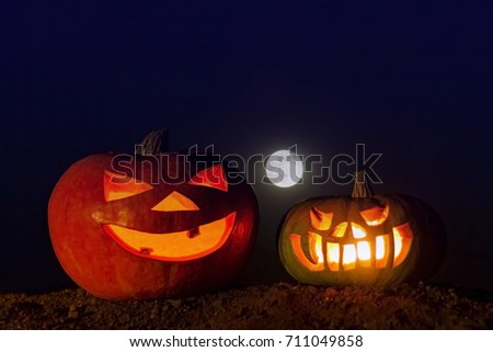 Two glowing pumpkins on the ground and a full moon in the dark blue sky. Picture for decoration on the holiday of Halloween.