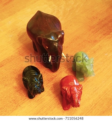 Herd of 4 stone elephants made from precious stones and wood walking on a wooden table.