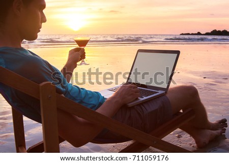 successful businessman freelancer working on computer at sunset beach, laptop with empty screen and copyspace