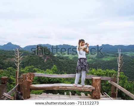 Portrait picture of a beautiful Eurasian girl / lady / woman tourist taking photos of mountainous scenery as an activity in community-based tourism (CBT) in Mae Hong Son province, Thailand.