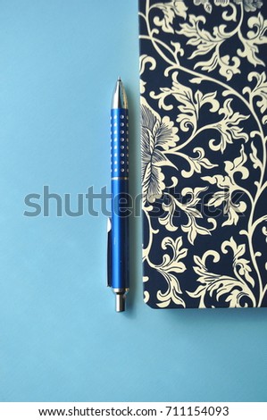 Dark blue floral notebook with blue pencils, white and blue background and copy space